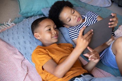 Siblings relaxing on cushions using digital tablet at home