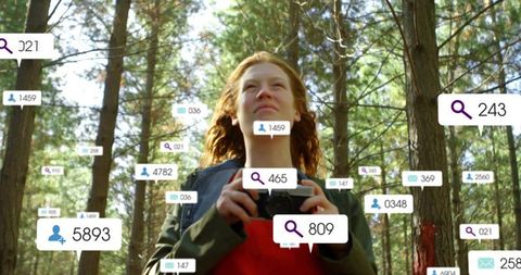Young woman holding dslr in sunlit pine forest with floating social media ui tags