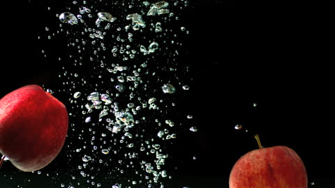 Red Apples Plunging Into Splashing Water Against Black Background