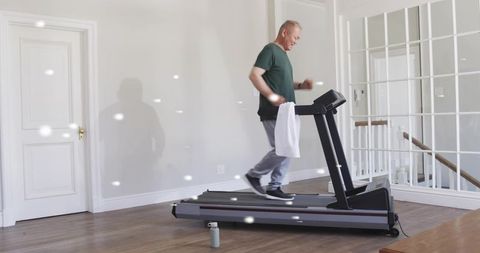 Mature man walking on home treadmill in modern minimalist room with towel and water bottle
