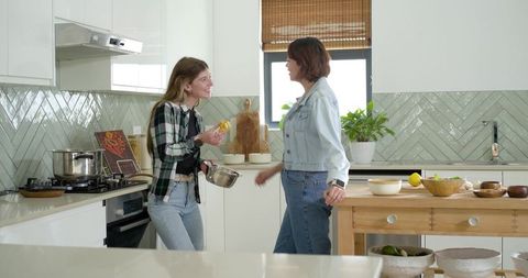 Diverse friends chatting and cooking in bright kitchen, chopping lemons and mixing batter
