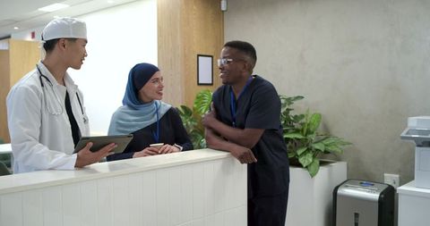 Multicultural medical team talking at reception desk consulting tablet and sharing coffee