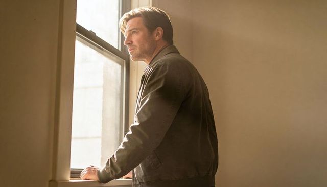 Contemplative middle-aged man standing at sunlit window hands on sill quiet reflection