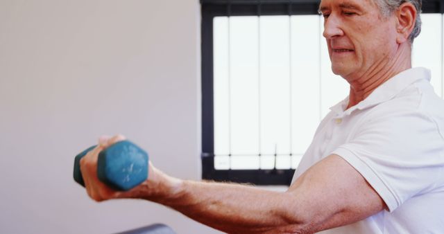 Senior man lifting weights in a home setting, focusing on fitness and maintaining a healthy lifestyle. Exercising with dumbbells to build strength and stay active. Ideal for articles or blogs about senior fitness, healthy aging, home workouts, and promoting an active lifestyle for older adults.