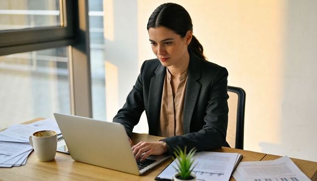 Focused professional typing on laptop at modern wooden desk in bright office workspace