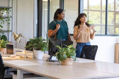 Diverse female coworkers collaborating in open-plan office with greenery and natural light