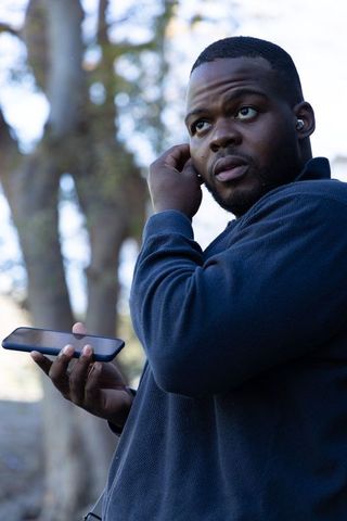 African american man adjusting earbud while holding smartphone outdoors in nature