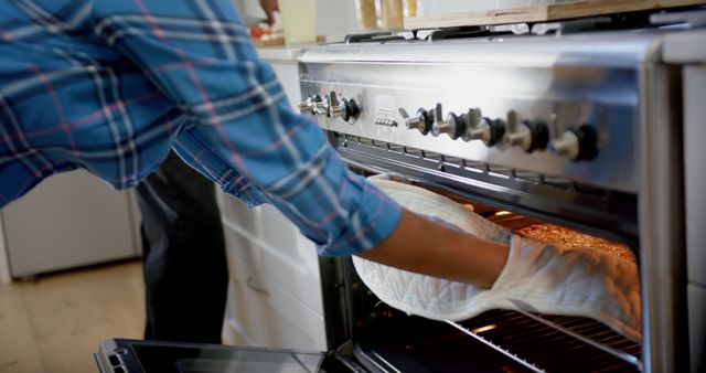 Person checking their cooking in the oven while wearing an oven mitt. Suitable for content related to home cooking, baking tutorials, kitchen safety, culinary classes, and domestic life.