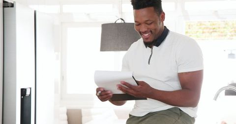 Smiling Man Writing on Clipboard in Modern Kitchen