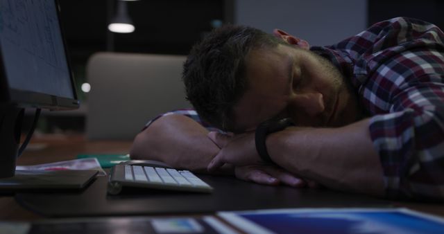Exhausted Caucasian man rests at his office desk. Overwork leads to fatigue, evident in the slumped posture and dim office setting.