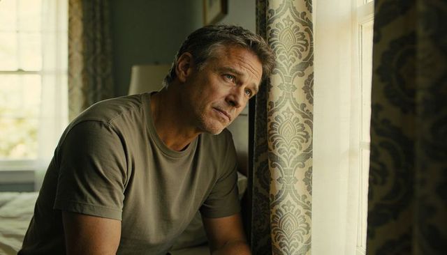 Middle-aged man gazing out bedroom window contemplative sunlit home reflection