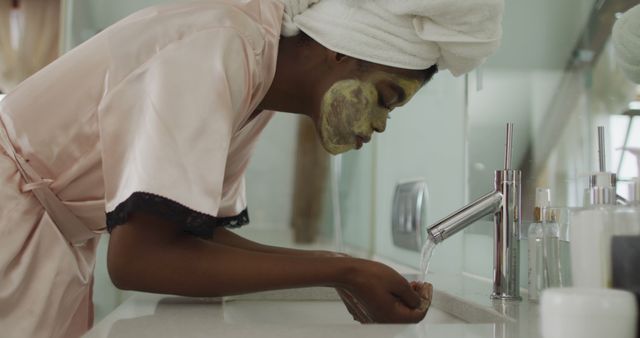 African american attractive woman washing off face mask in bathroom. beauty, pampering, home spa and wellbeing concept.