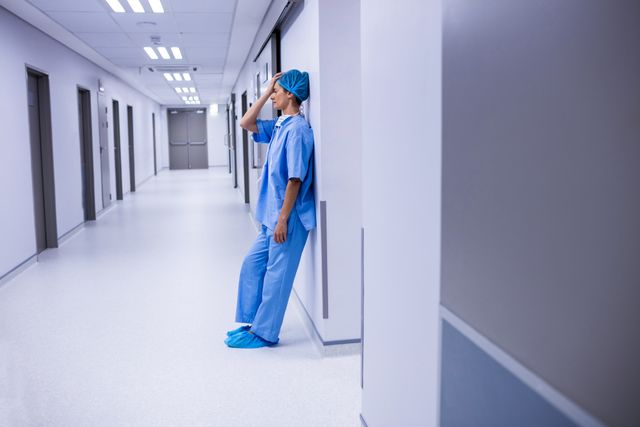Sad surgeon leaning on wall in corridor at hospital