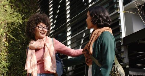 Female students laughing and chatting on university campus with backpacks and scarves