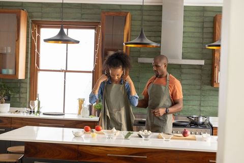 Couple preparing meal on modern wooden kitchen island tying aprons and arranging ingredients