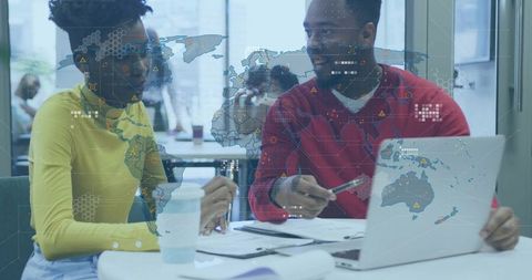 Young professionals collaborating over laptop with global data overlay in modern office