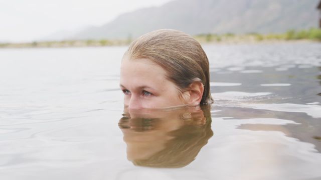 Caucasian woman immersed in water while swimming in a serene mountain lake. Perfect for promoting outdoor adventure, travel destinations, healthy lifestyle, relaxation, and wilderness escapes.