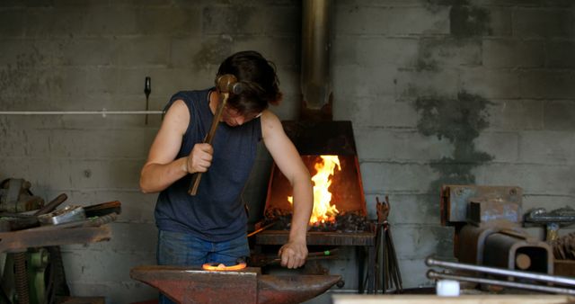 Blacksmith Wearing Sleeveless Shirt Hammering Glowing Metal in Workshop - Download Free Stock Images Pikwizard.com