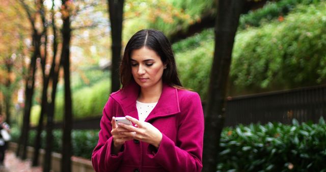 Woman in Pink Coat Texting on Smartphone in Park - Download Free Stock Images Pikwizard.com