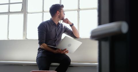 Contemplative Young Professional with Laptop by Office Window