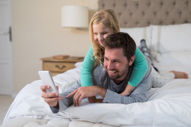 Father and daughter taking a selfie on bed