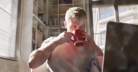 Man Drinks Coffee While Using Laptop in Cozy Home Office