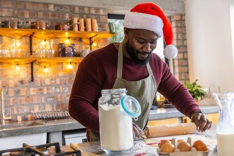 African american man baking holiday cookies in cozy rustic kitchen wearing santa hat