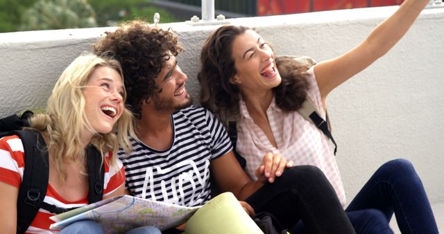 Three friends are joyfully taking a selfie while on a travel adventure. One is holding a map, indicating their excitement for exploring new places. Great for use in travel promotions, friendship and adventure themes, or marketing youthful, carefree experiences.
