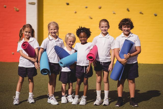 Portrait of smiling schoolgirls standing with exercise mat in schoolyard