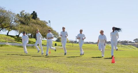 Female Athletes Running Across Field in White Training Uniforms