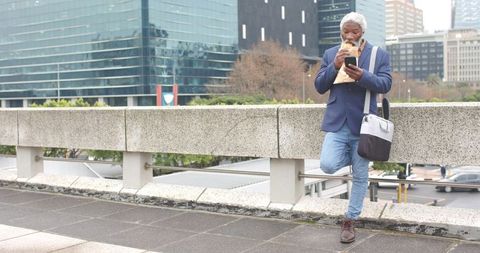 Mature african-american professional eating sandwich while checking phone on city overpass
