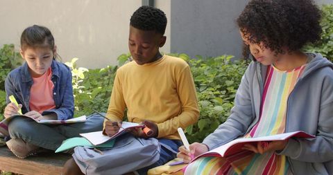 School-age students studying outdoors, writing notes and highlighting in notebooks