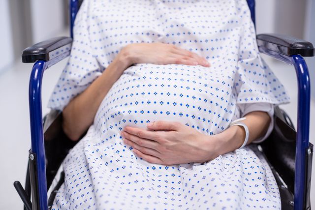 Mid section of pregnant woman sitting on wheelchair in hospital