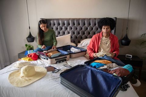 Diverse couple organizing suitcase for vacation in modern hotel room
