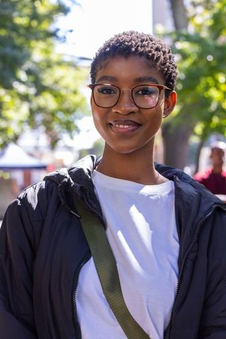 Confident smiling african woman wearing glasses and puffer jacket on sunlit urban street