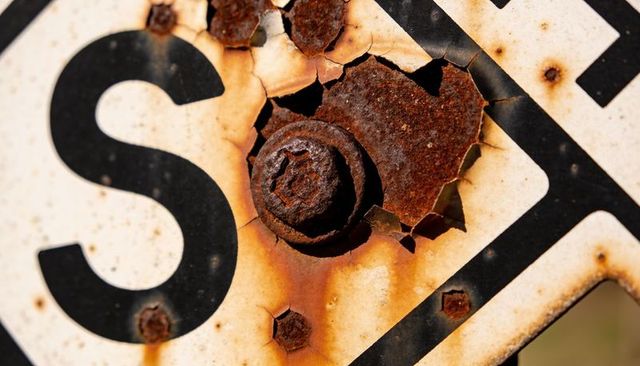 Rusted bolt peeling paint and flaking patina on weathered roadside sign close-up