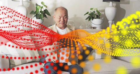 Senior man using tablet at home with flowing red and yellow digital data wave overlay