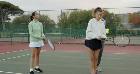 Female tennis teammates practicing on hard court, training together and collecting balls