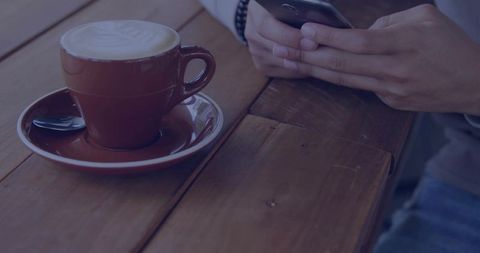Man checking smartphone beside latte on wooden table with bracelet and watch
