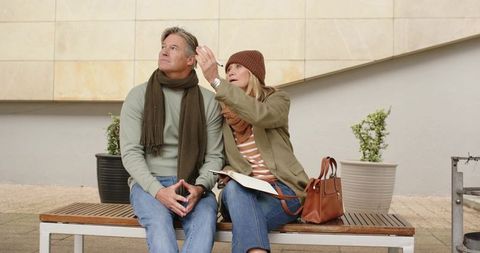 Mature couple planning route on map while sitting on bench in urban courtyard