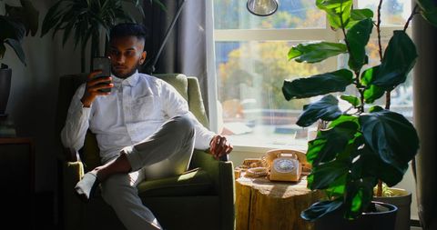 Young man relaxing with smartphone in sunlit living room