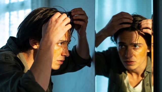 Adjusting hair in mirror at home, intense grooming portrait with yellow face mark
