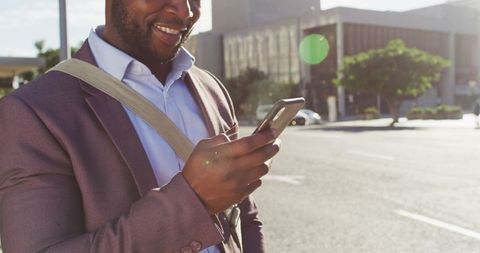 African American Man Smiling While Using Smartphone on City Street