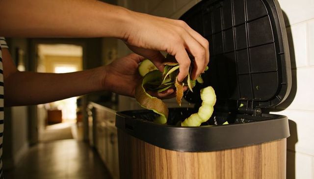 Hands dropping apple peels into woodgrain kitchen bin for home composting and food waste reduction