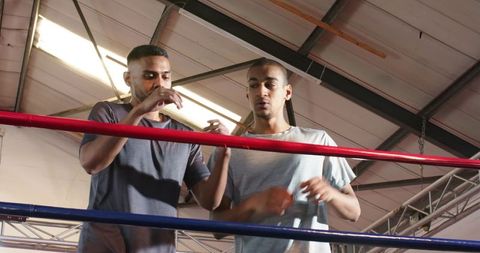 Boxing training partners adjusting gloves in industrial gym ring under skylight