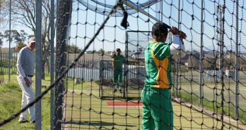 Cricket batting practice in nets with coach supervising players during outdoor training