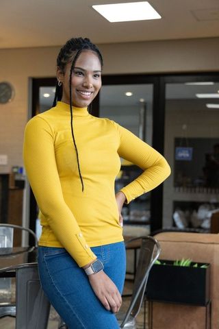 Smiling african american woman posing in coworking cafe wearing yellow turtleneck and smartwatch