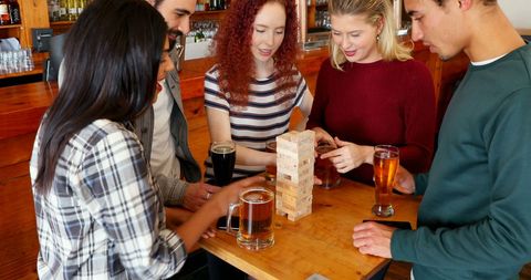 Friends Enjoying Jenga Game and Drinks at Bar Gathering