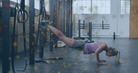Performing suspended decline push-up with feet in straps and rings in crossfit gym