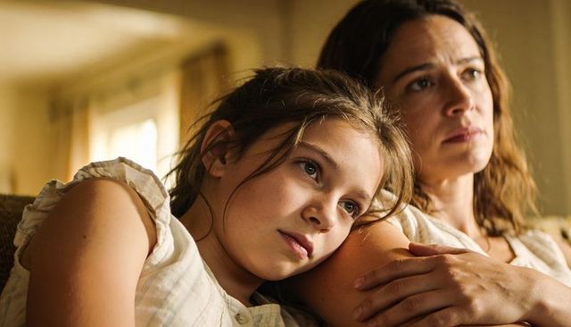 Mother and daughter sharing quiet moment on sofa, intimate bonding in warm sunlit home